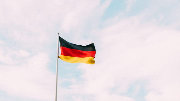Eine Deutschlandflagge weht an einem sonnigen Tag vor blauem Himmel mit weißen Wolken.